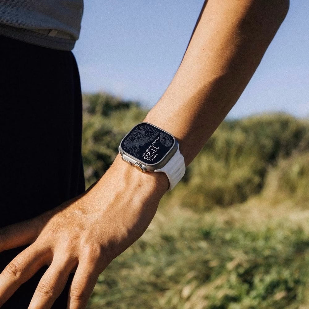 Смарт-годинник Apple Watch Ultra з білим перфорованим ремінцем на фоні ландшафту, надійне кріплення та комфортна посадка на руці