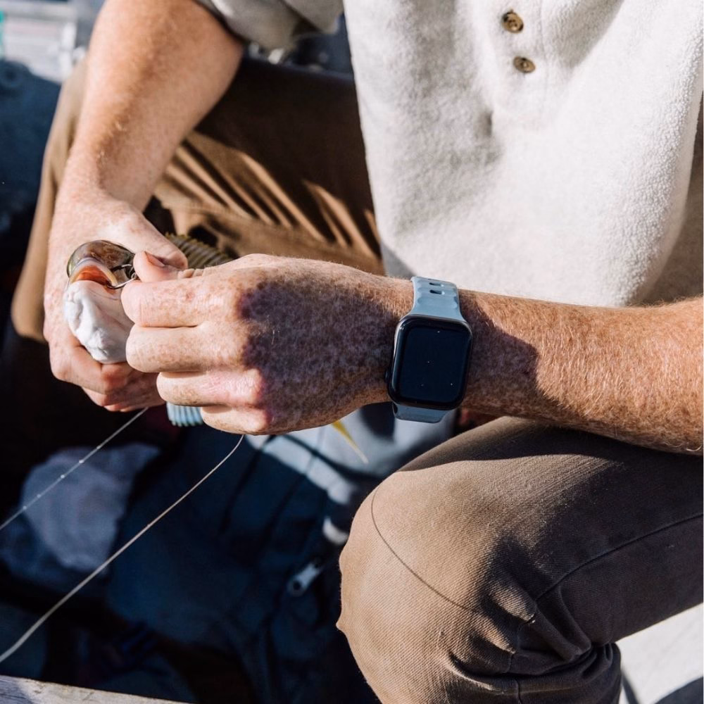 Синій силіконовий ремінець Nomad Sport Band Marine Blue на руці рибалки під час зняття гачка з риби