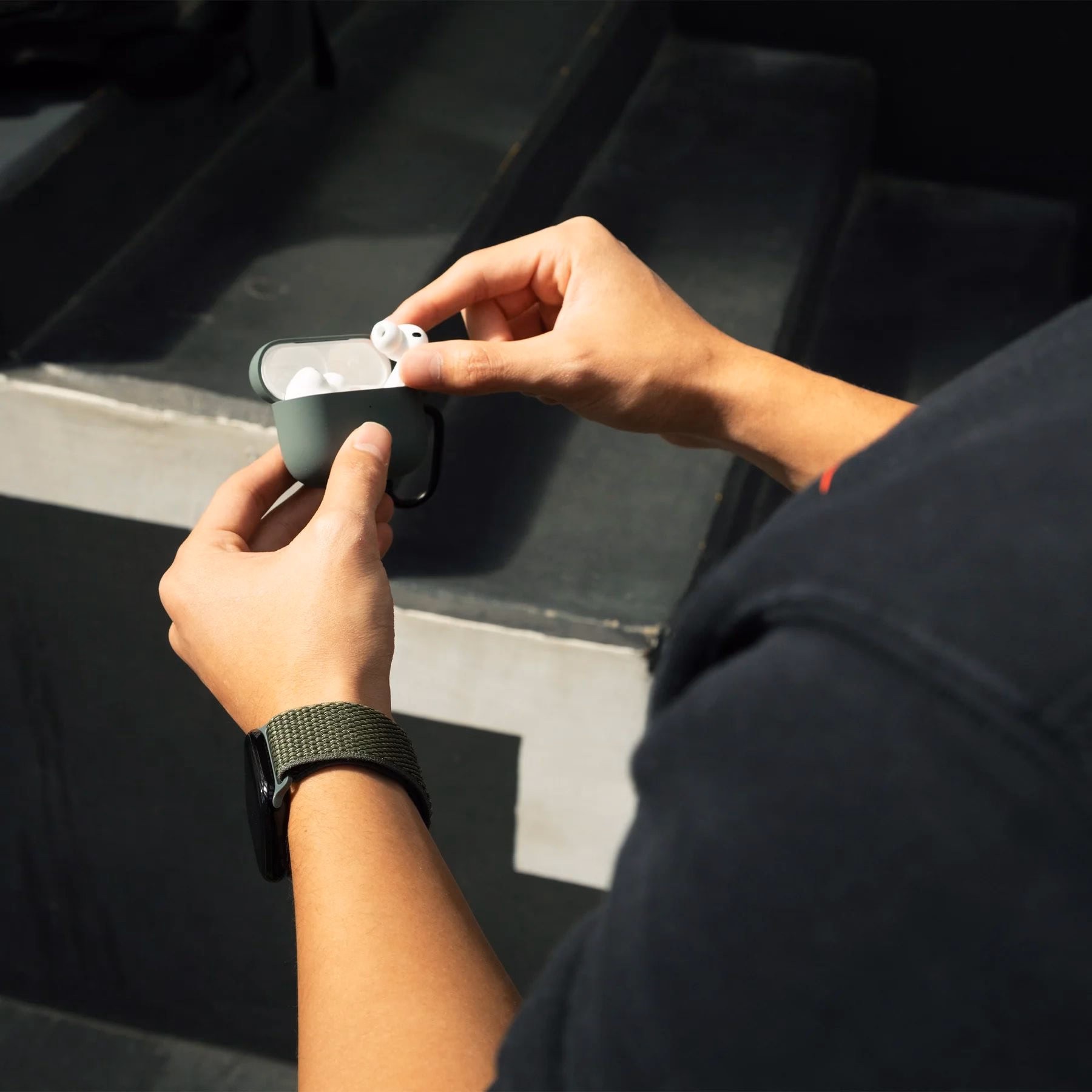 Чоловіча рука з ремінцем Slate Green поруч із чохлом для AirPods
