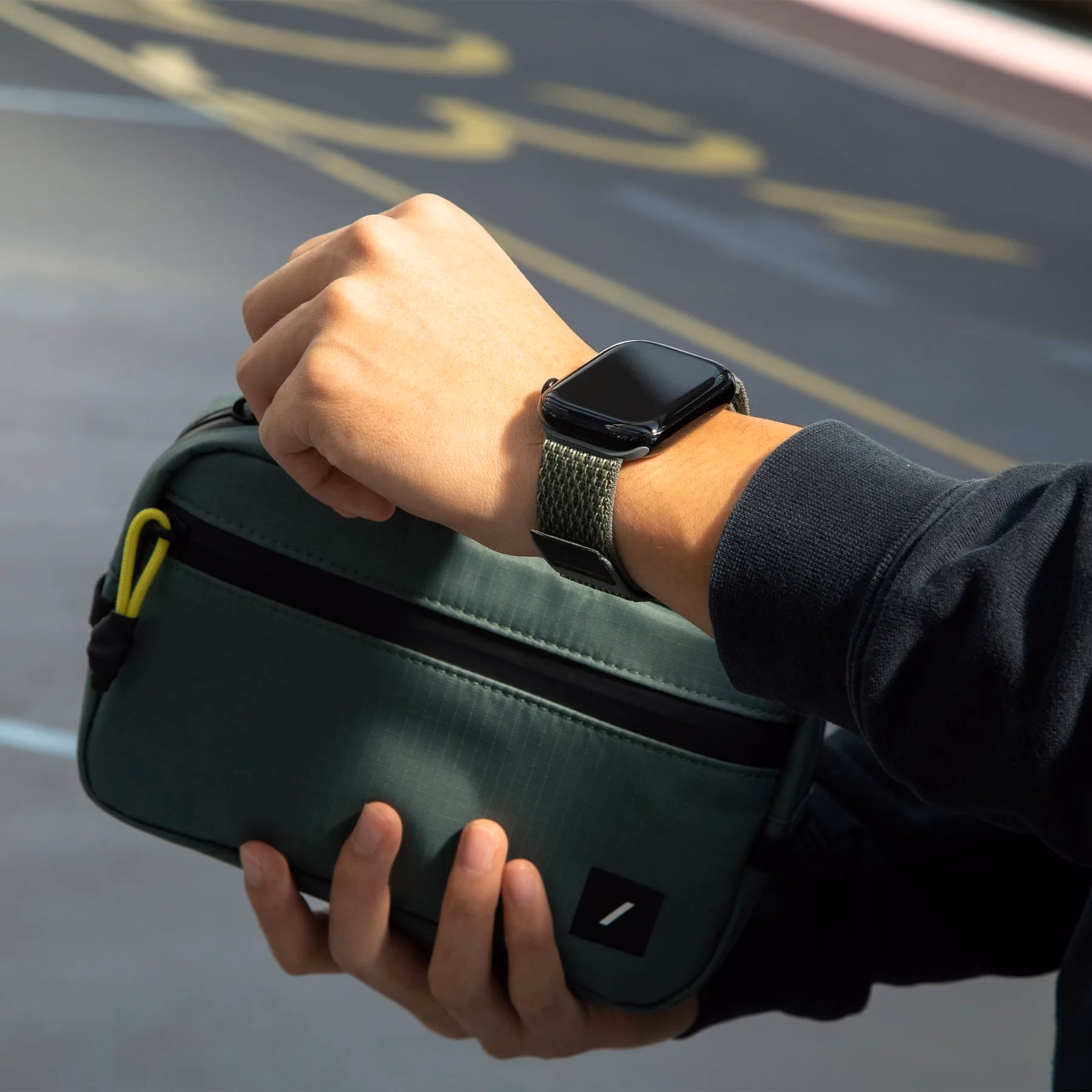 Ремінець Native Union Slate Green на руці поруч із сумкою-косметичкою