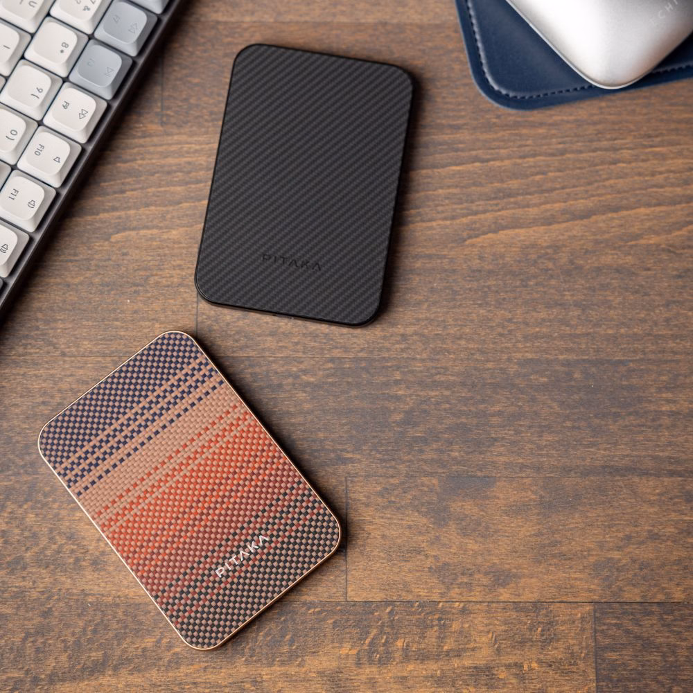 Портативна батарея Pitaka Aramid Fiber Qi2 10000mAh у кольорах Sunset та Black з преміального арамідного волокна на дерев'яному робочому столі