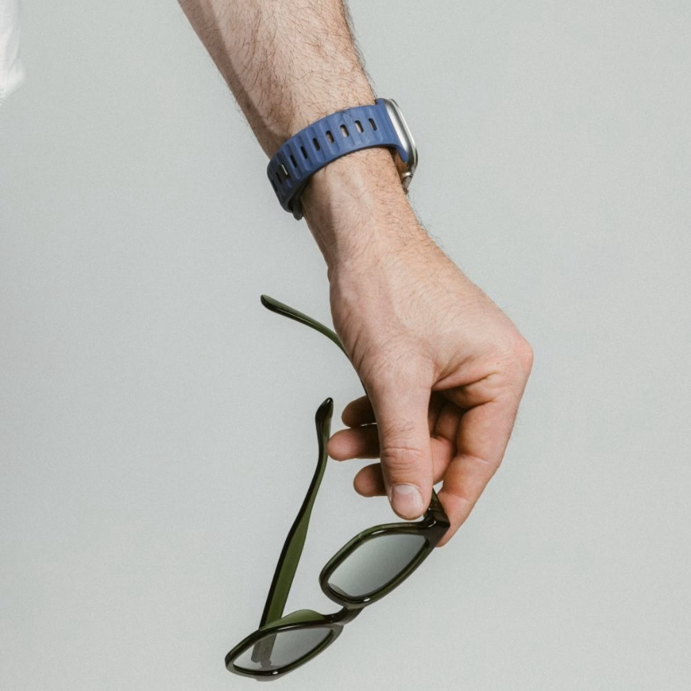 Синій спортивний ремінець Nomad Sport Band Naval Blue з FKM фтореластоміру на руці користувача, що тримає окуляри, для Apple Watch Ultra 49mm